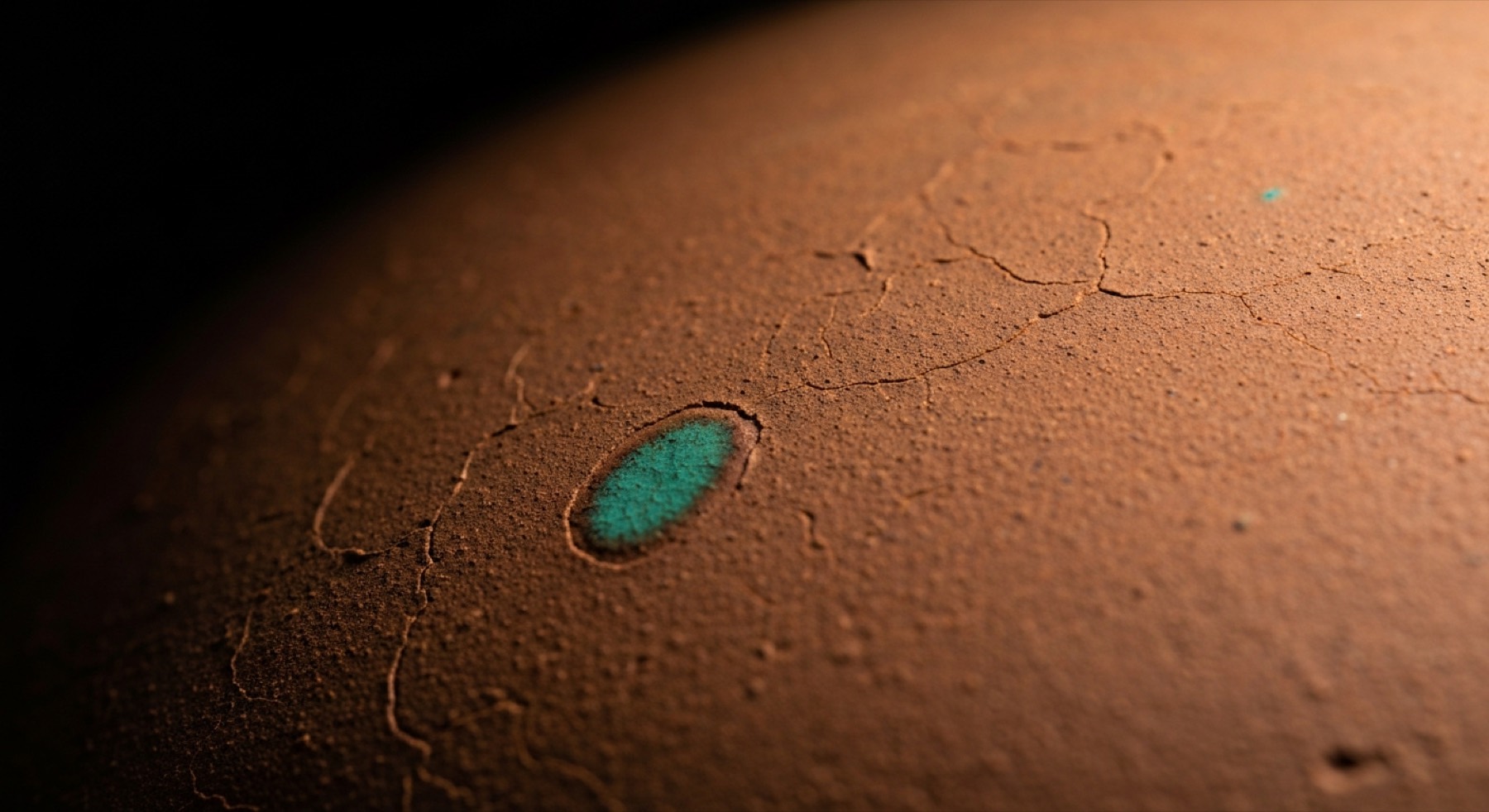 A fired clay surface, cracked with age, with one small inlay of teal glaze set into it.