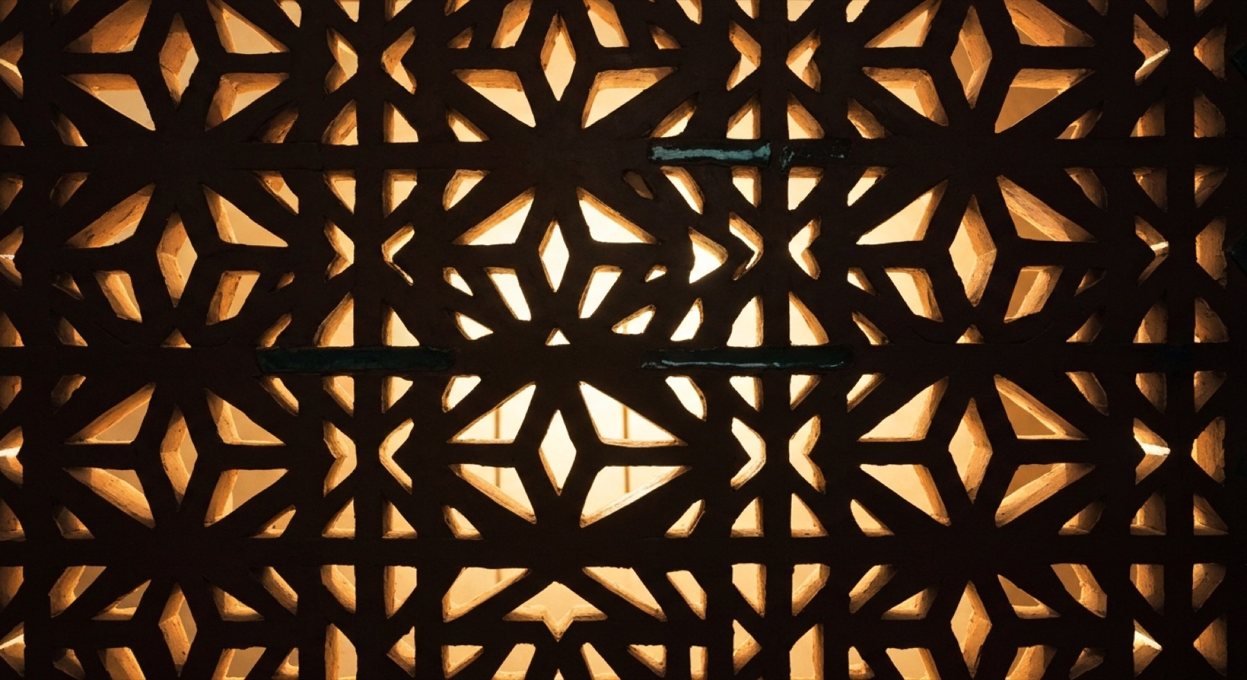 A pierced stone screen lit from behind, its repeating star pattern arriving as points of light rather than as an even wash.