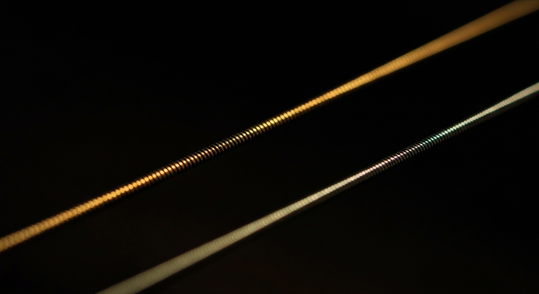 Two strings side by side against a black ground. One catches
  a warm light along its whole length; the second falls almost entirely into shadow.
